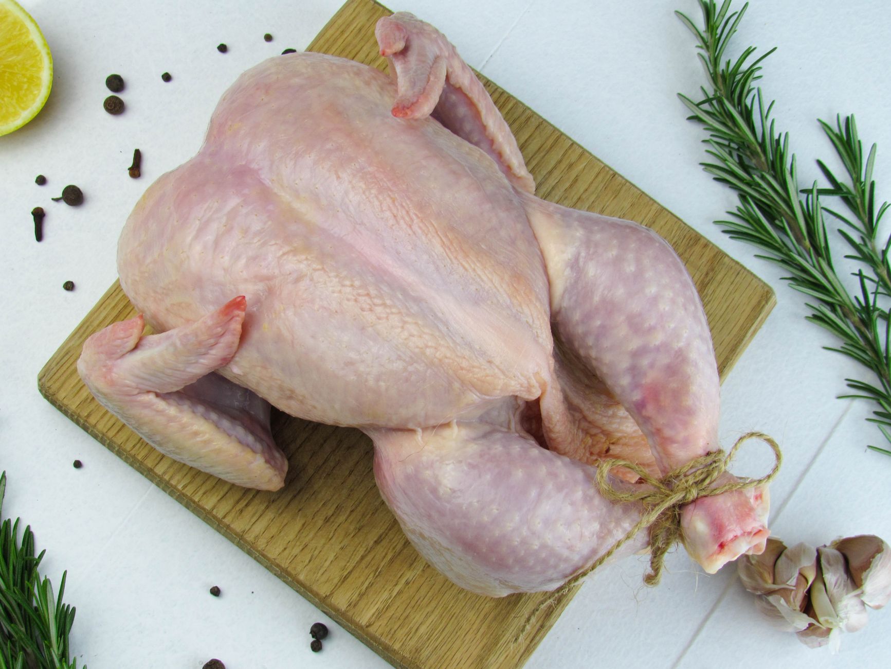 A whole raw chicken with rosemary on a wooden board