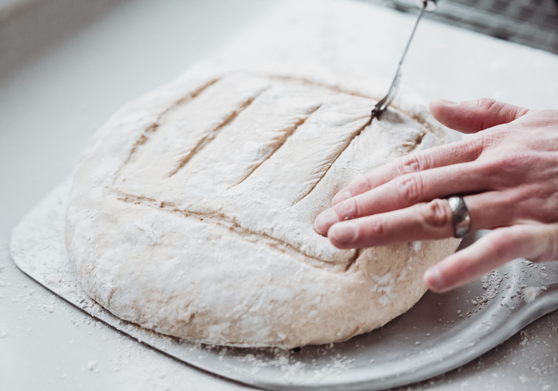 Hands scoring a loaf before it goes in the oven