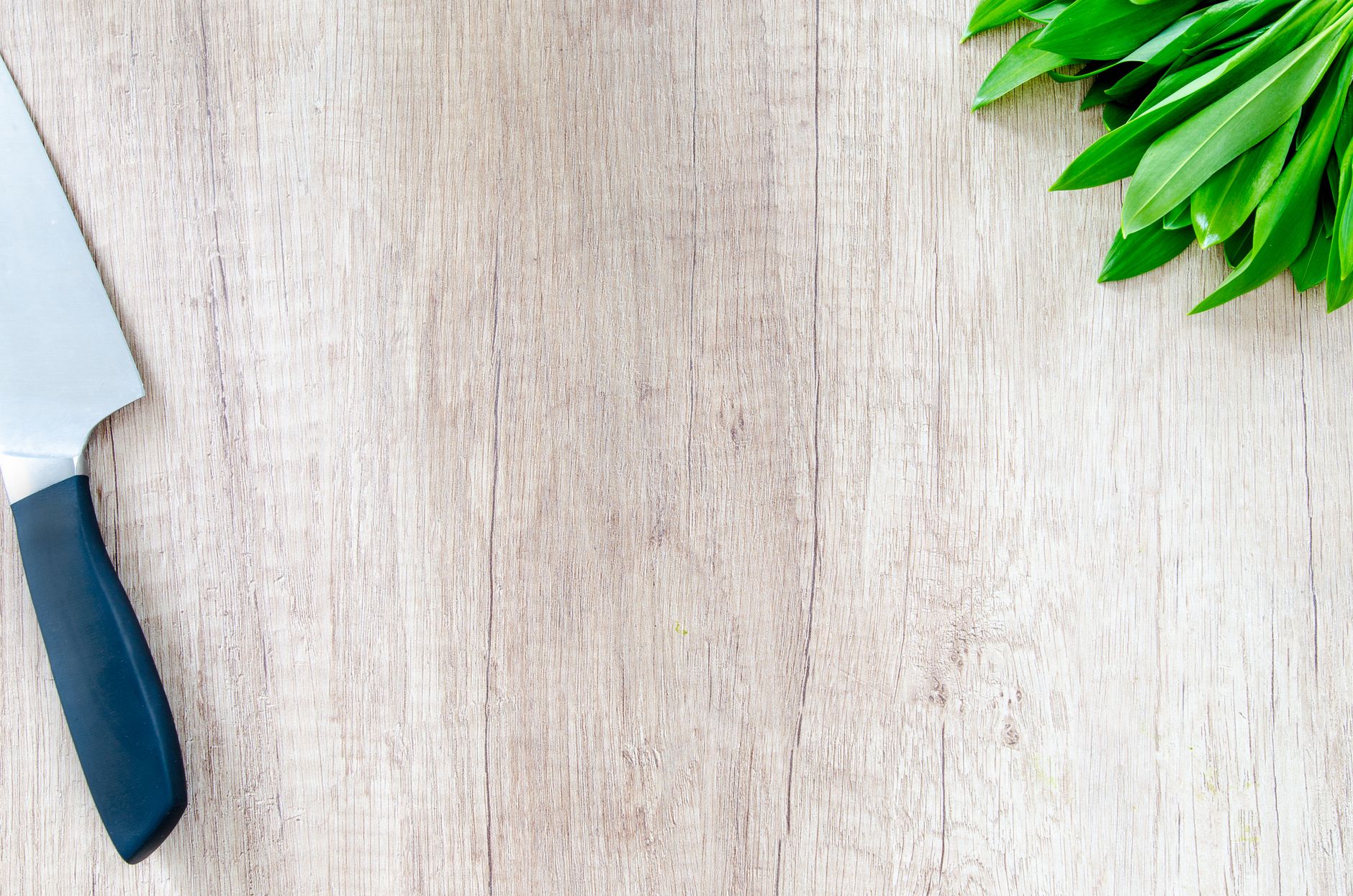 A chef knife and fresh herbs on a wooden bench