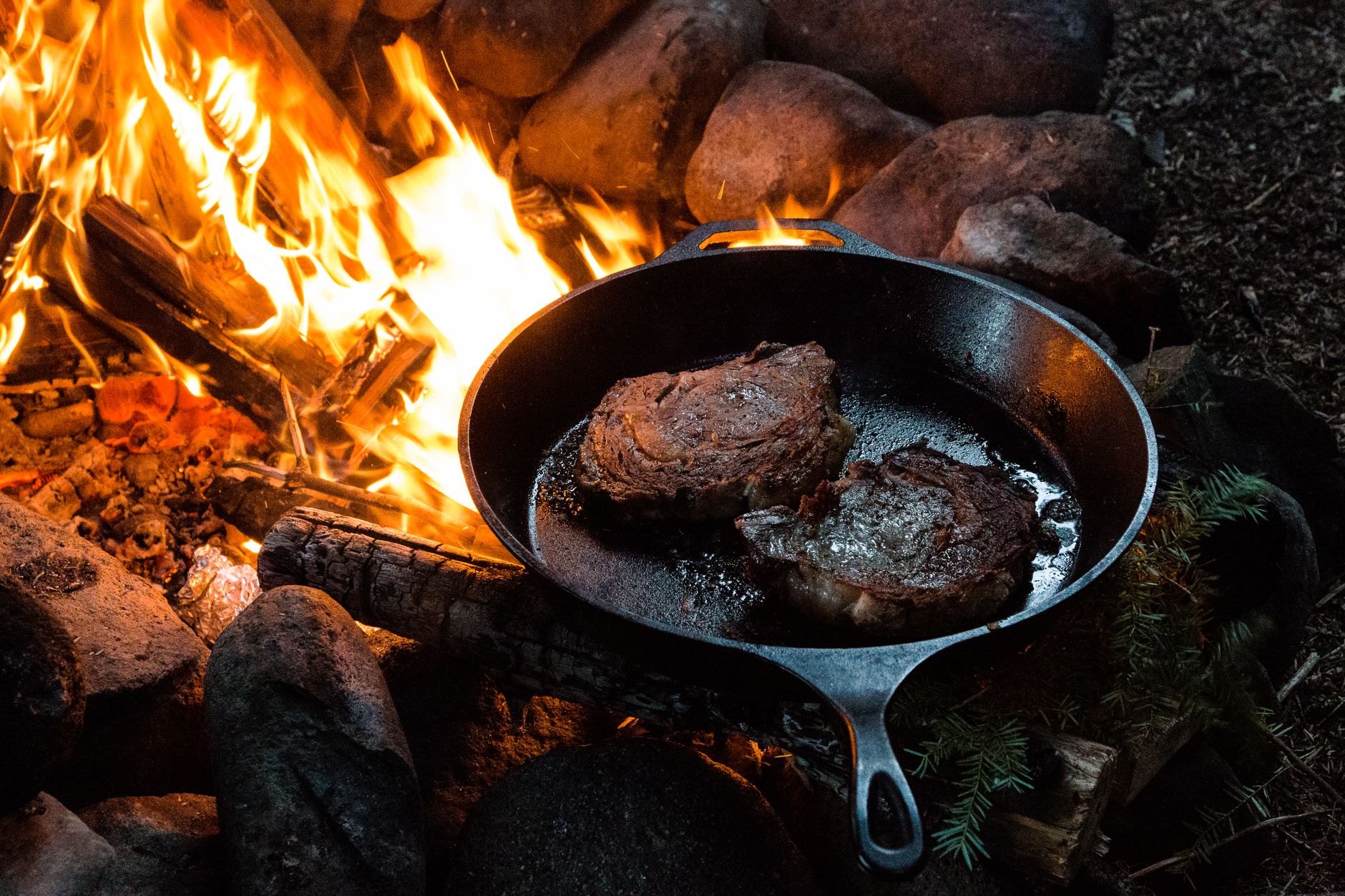 Steaks searing in a cast iron pan over fire